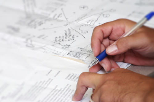 Working on blue print document Closeup photo of man working on architectural project, going over check list.